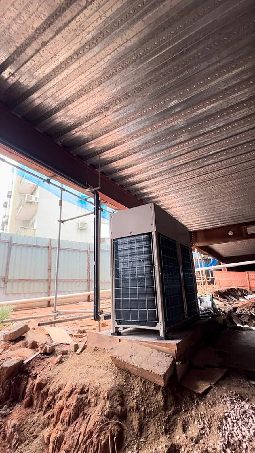 Unidade condensadora Daikin sobre base, sob a laje metálica de uma obra em andamento