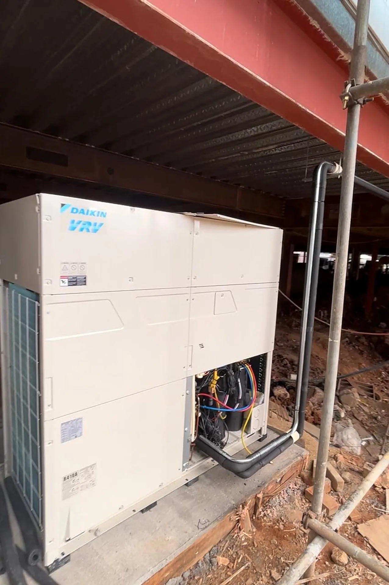 Unidade condensadora Daikin VRV sobre base de concreto, com tubulação isolada e andaime ao lado