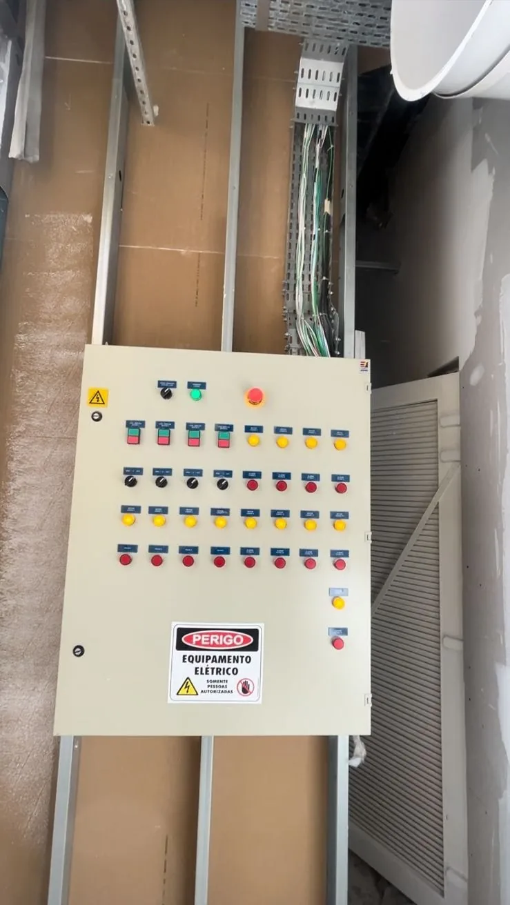 Quadro de comando elétrico com botões, sinaleiras e placa de perigo, instalado em parede