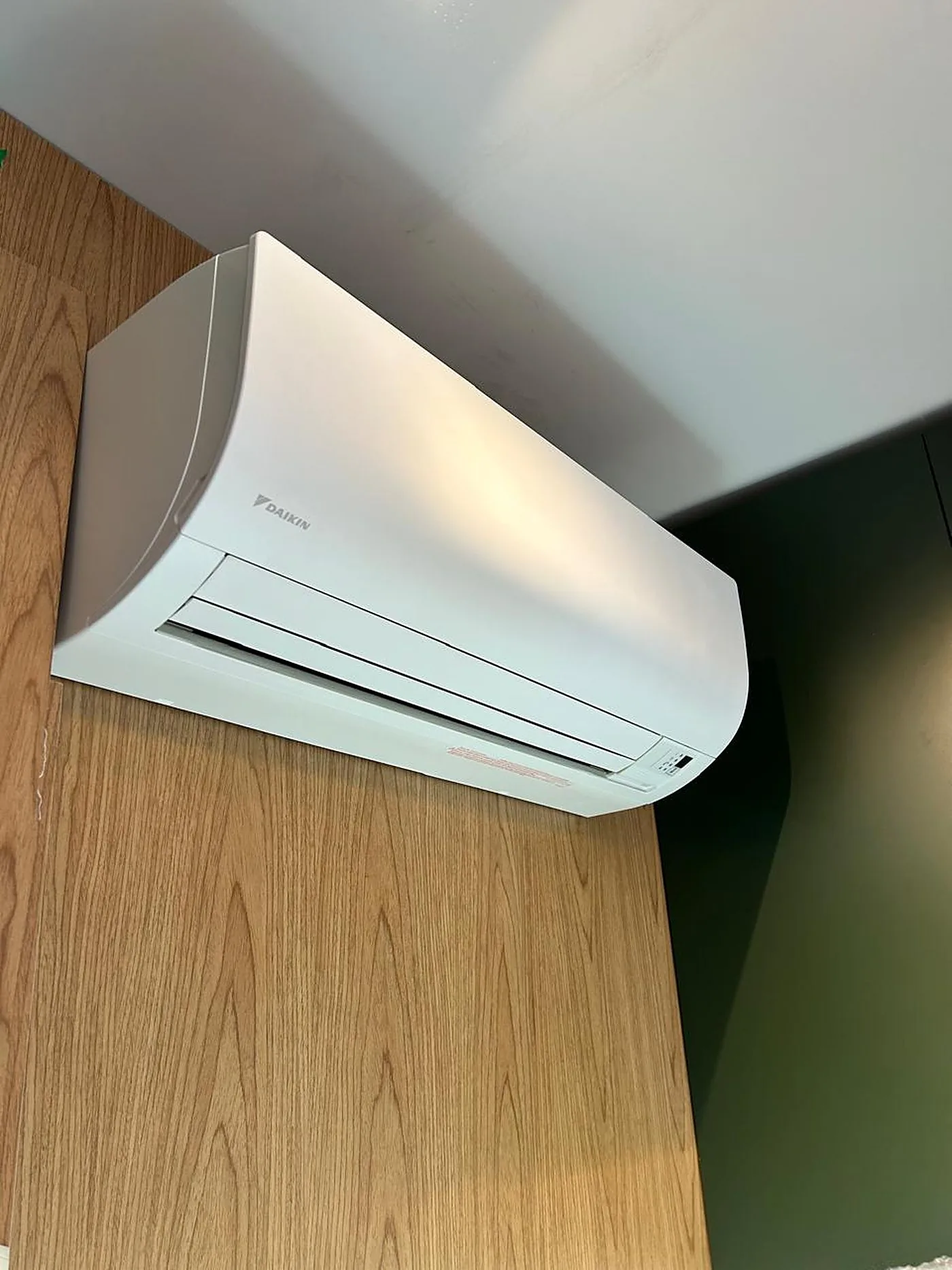 Detalhe de um split Hi-Wall Daikin instalado em painel de madeira, ao lado de uma parede verde