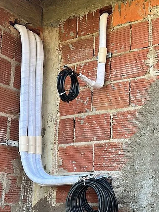 Tubulação frigorífica isolada e cabos de interligação enrolados, fixados em parede de alvenaria