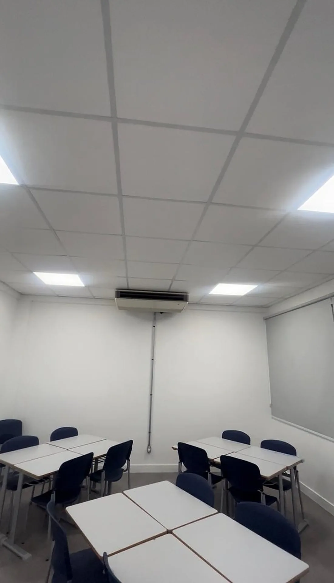 Unidade interna de climatização instalada no teto de uma sala de aula com forro modulado